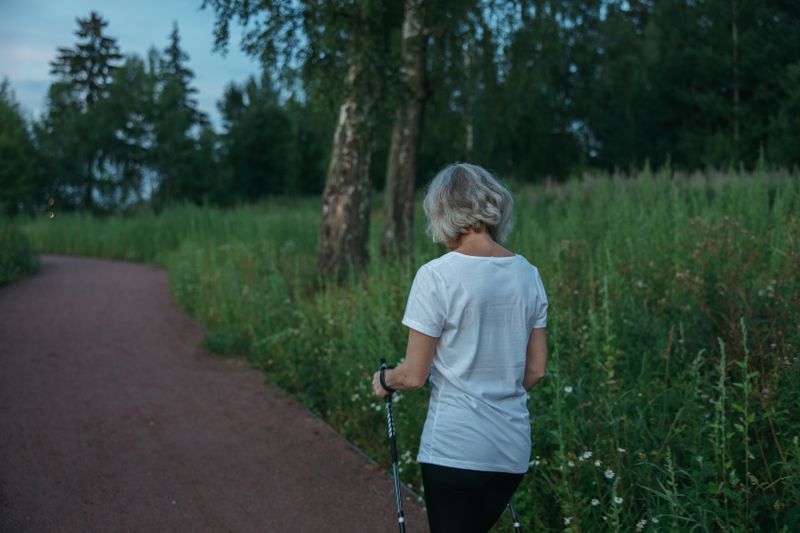 An older woman nordic walking through a park